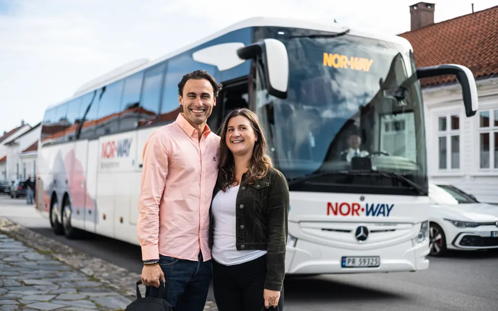 mann og kvinne smiler foran nor-way buss i koselig trehusgate