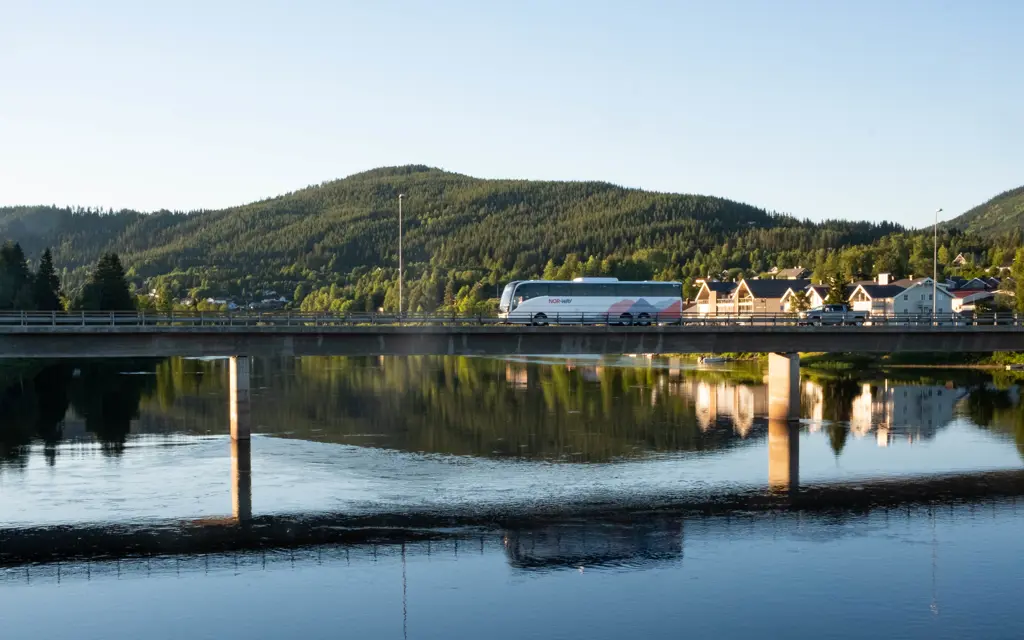 NOR-WAY buss kjører over en bro med refleksjon i vannet under