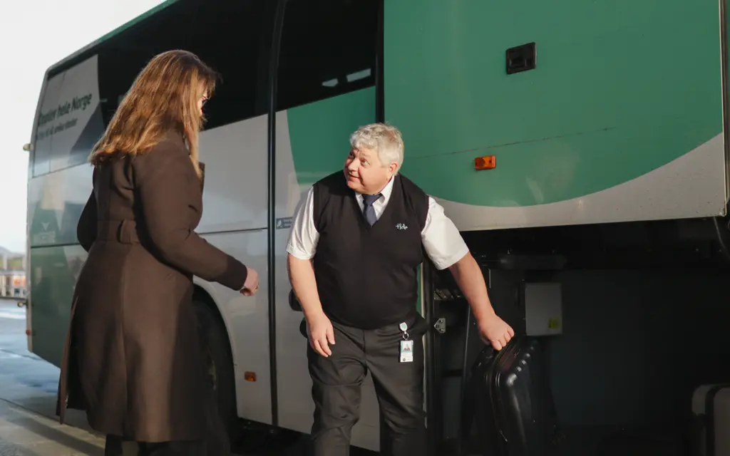 Passasjer får koffert av sjåfør utenfor flybuss