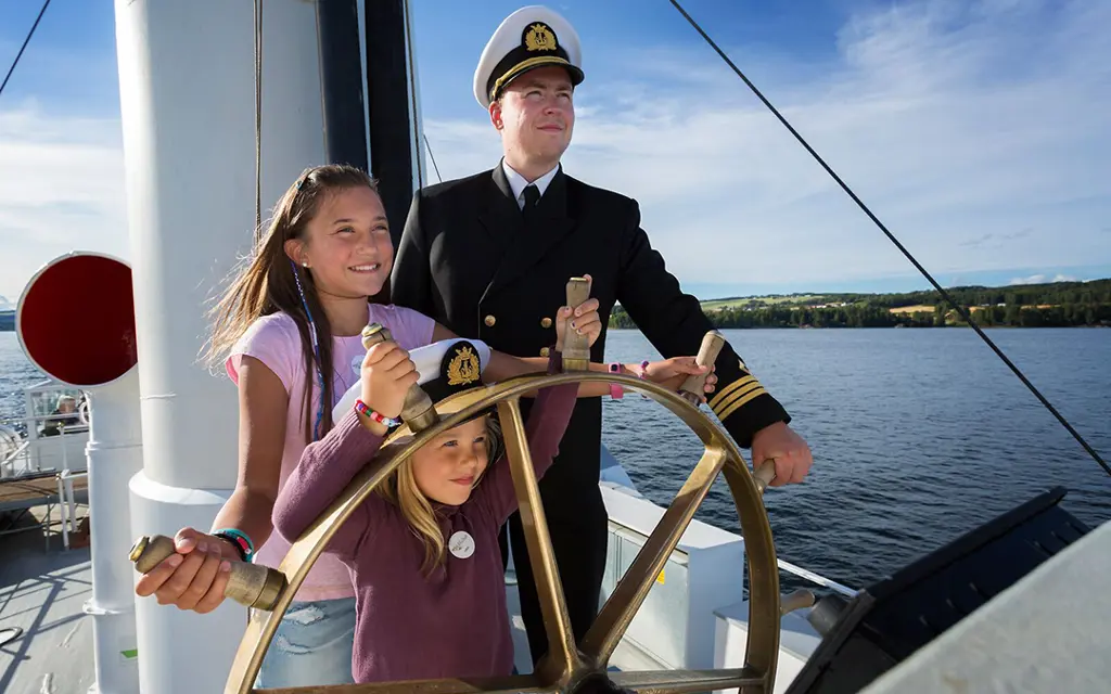 A skipper together with two kids on board of Skibladner