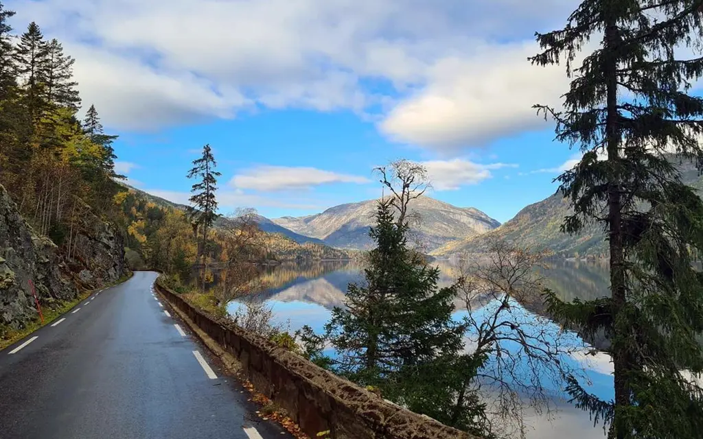 Bilvei ved stille vann og fjellandskap