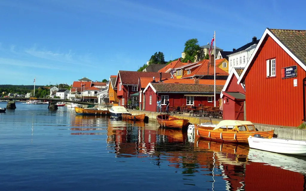 Rød- og hvitmalte hus langs bryggekanten med båter i front