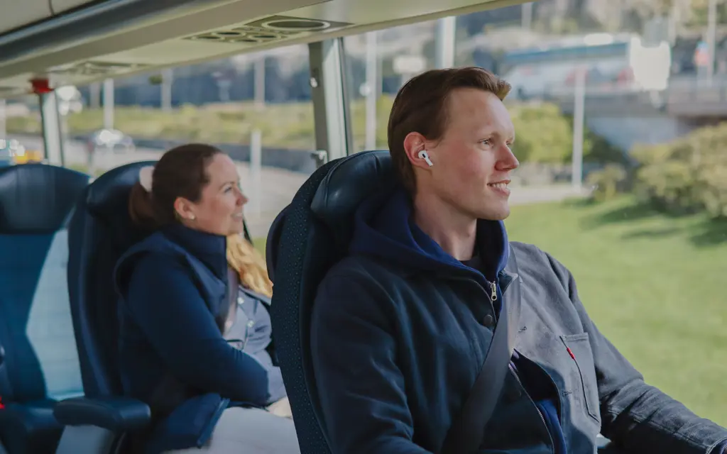 Smilende passasjerer ombord i buss, med NOR-WAY buss i bakgrunnen