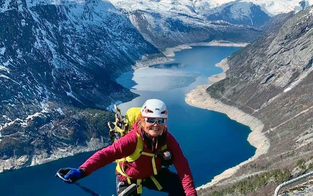 Fjellklatrer på vei opp fjellsiden med fjord og fjell i bakgrunnen
