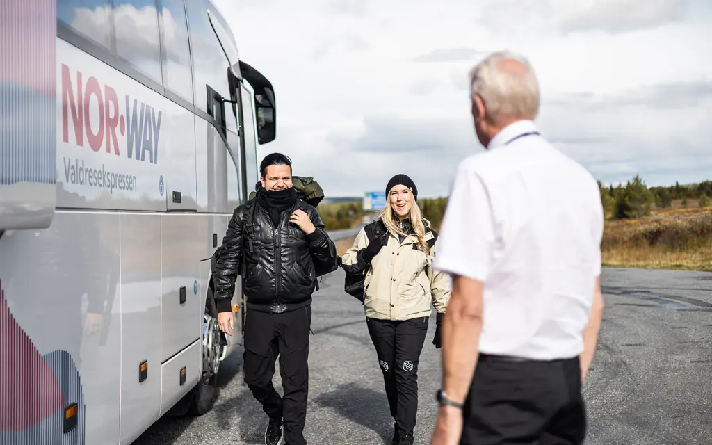 man and woman walking outside Valdresekspressen towards a bus driver