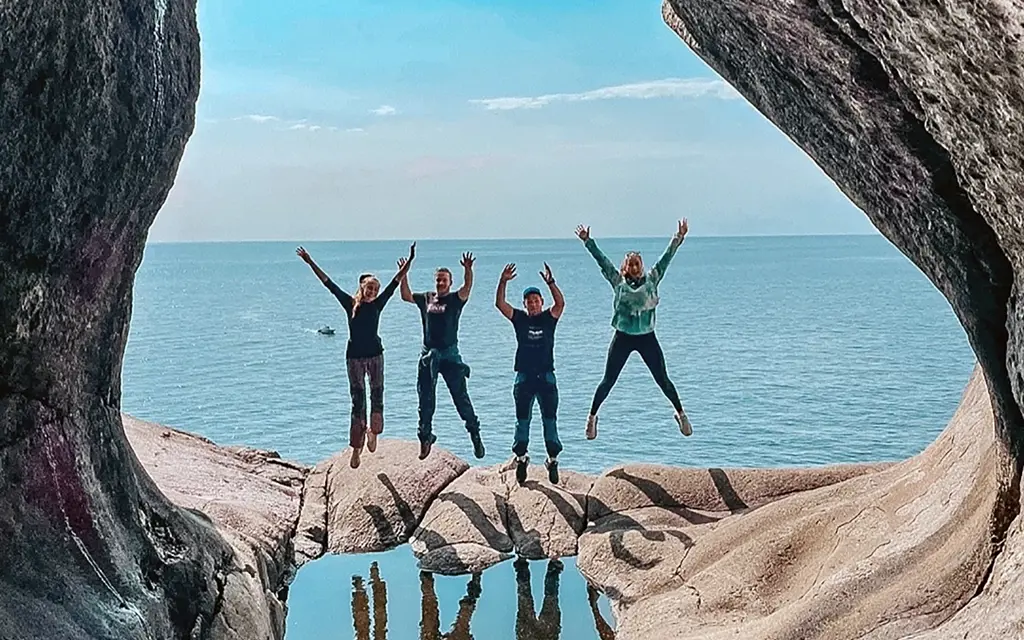 From a cave in the mountains, we see four jumping people in front of the sea