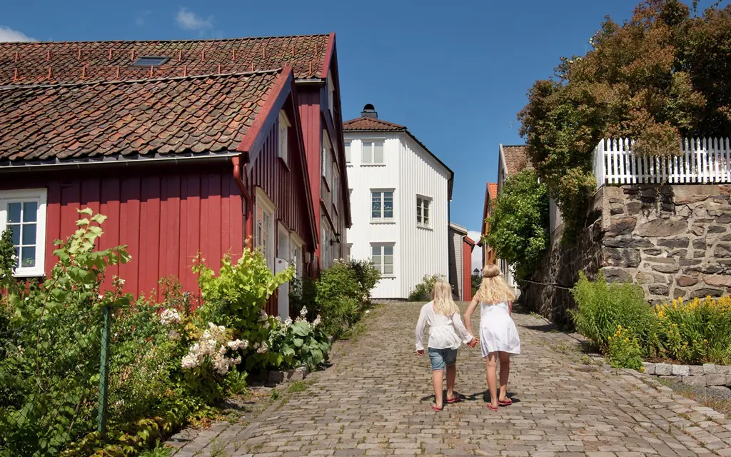 Et rødmalt og hvitmalt hus langs brosteinsgater med to barn gående