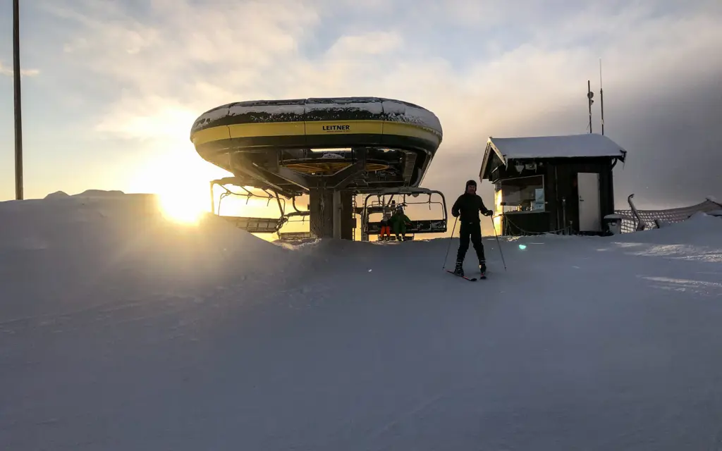 Mann står på ski ved en skiheis hvor solen titter frem over horisonten