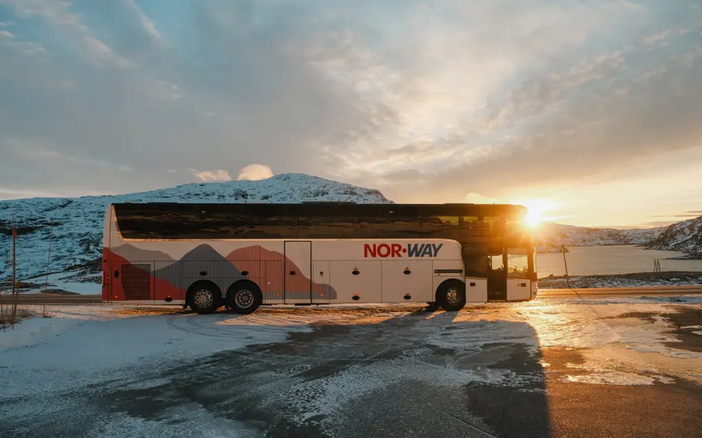 Buss fra NOR-WAY med snø og is i bakgrunnen og solen som titter frem bak bussen