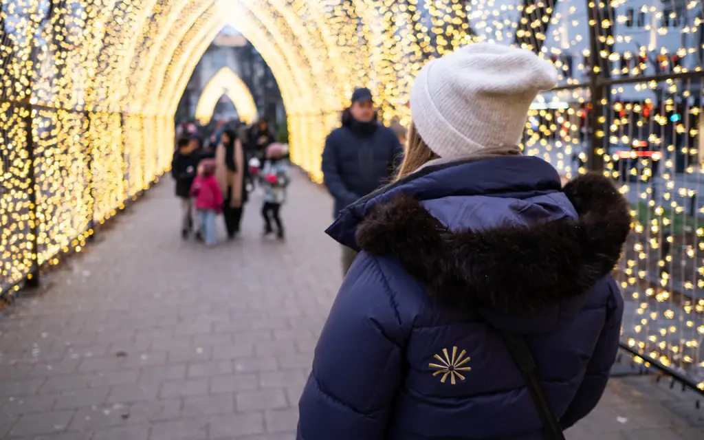 Kvinne i blå jakke med grå lue står i en lysbue på julemarked